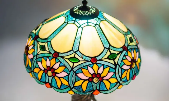 Lampe vitrail aux motifs floraux colorés, avec des pétales jaunes, roses et bleus, et des cabochons rouges et verts.