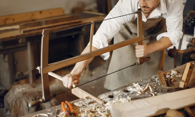 Artisan menuisier travaillant le bois avec une scie, dans un atelier d'ébénisterie d'art.