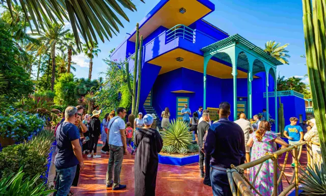 Visiteurs admirant l'architecture vibrante et la végétation luxuriante du jardin Majorelle, un havre de paix bleu cobalt et jaune.