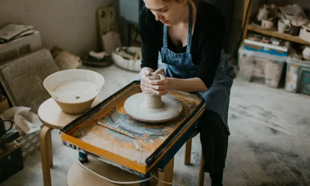 Jeune femme concentrée sur son apprentissage de l'artisanat de la poterie, façonnant l'argile sur un tour.