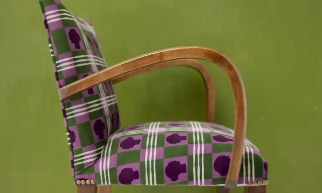 Fauteuil au motif écossais violet et vert, avec des silhouettes de têtes. Un bel exemple d'art tapissier.