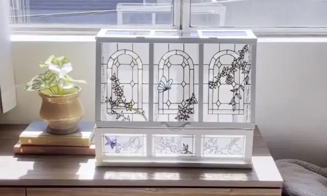 Boîte à bijoux ornée de vitraux décoratifs représentant des papillons et des fleurs, posée sur une commode en bois.