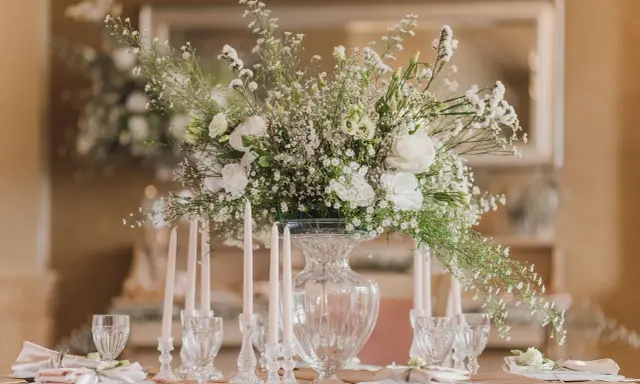 Un bouquet de vitrail fleur, blanc et aérien, orne une table dressée avec des bougies et des verres délicats.