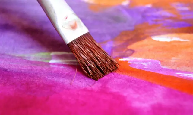 Pinceau humide sur une toile aux couleurs vives, mélangeant le pastel sec et l'eau pour créer des dégradés vibrants de rose, violet et orange.
