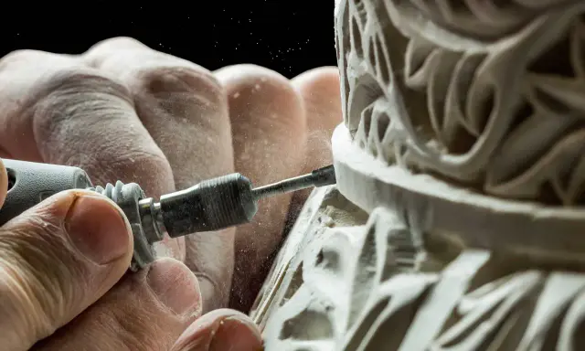 Mains habiles sculptant un ornement complexe, poussière fine dans l'air. Une image capturant la précision de la formation artisanat d'art.
