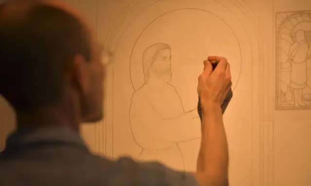 Un artiste esquisse un dessin vitraux, le visage de Jésus prenant forme sous son crayon.