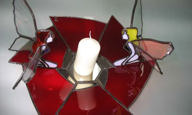 Un photophore vitrail aux couleurs vives, orné de deux anges aux ailes translucides, tenant une bougie blanche.