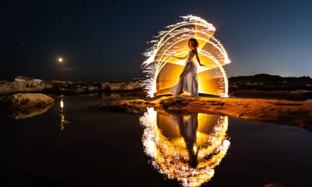 Une femme en robe blanche danse sous un ciel étoilé, entourée d'un halo de lumière incandescente, comme un **verre soleil** reflété dans l'eau.