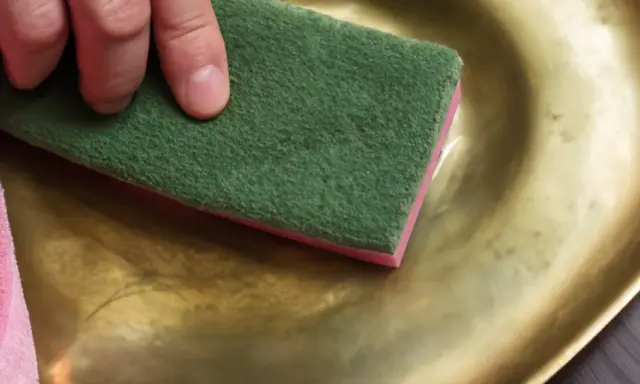 Main tenant une éponge verte et rose, une main frotte un plateau en cuivre jaune pour le nettoyer.
