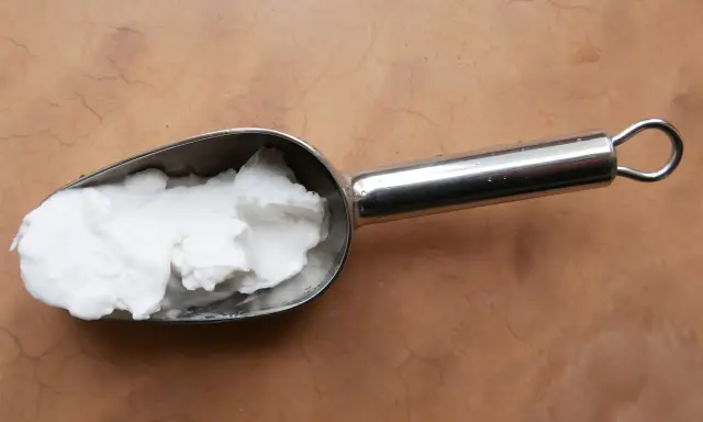 Une cuillère métallique contient une pâte blanche, peut-être de la cire saponifiée sur enduit chaux, prête à être appliquée.