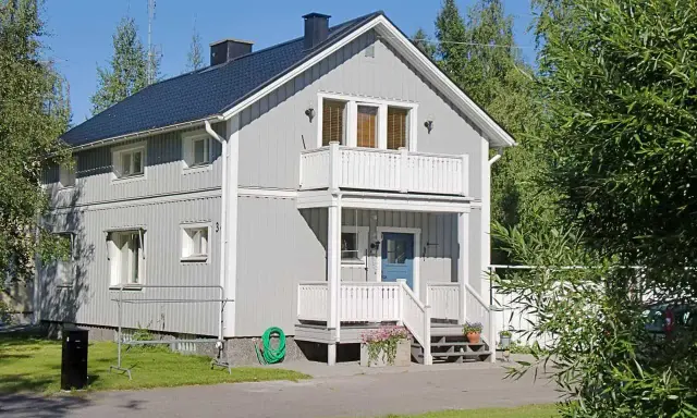 Maison à deux étages avec une peinture suédoise blanche, un balcon, une porte bleue et un jardin verdoyant.