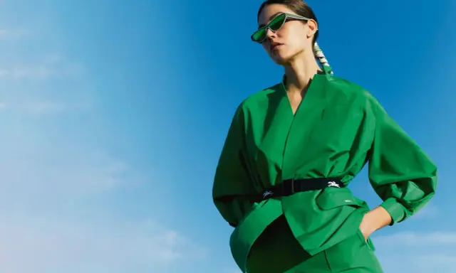 Une femme en tenue verte éclatante, lunettes de soleil futuristes, pose sous un ciel bleu. Un **cahier de tendance** inspirant.