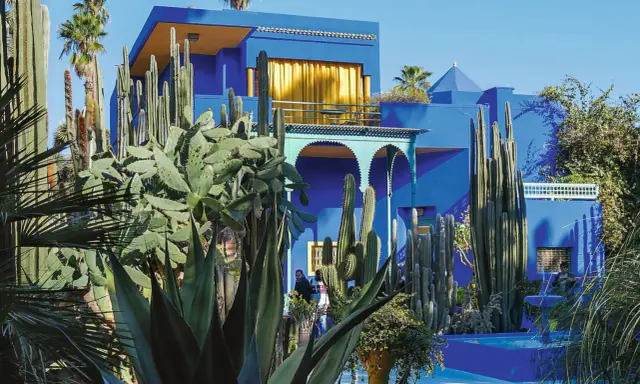 La **maison bleu Majorelle** se dresse fièrement, entourée d'une jungle de cactus et de palmiers. Un spectacle vibrant sous le ciel bleu.
