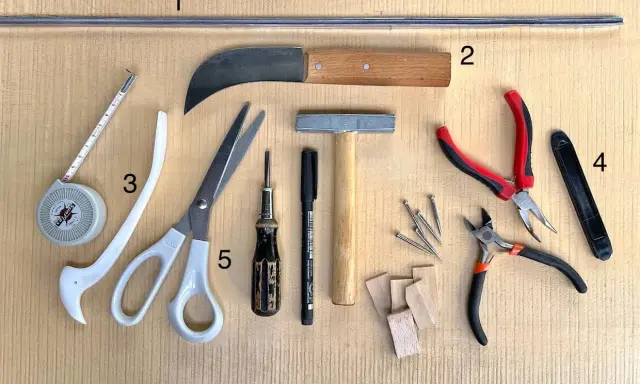 Outils pour le **matériel vitrail** : ruban à mesurer, ciseaux, couteau, marteau, pinces, clous et petits morceaux de bois.