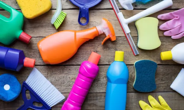 Divers produits et accessoires de nettoyage colorés sur fond de bois.