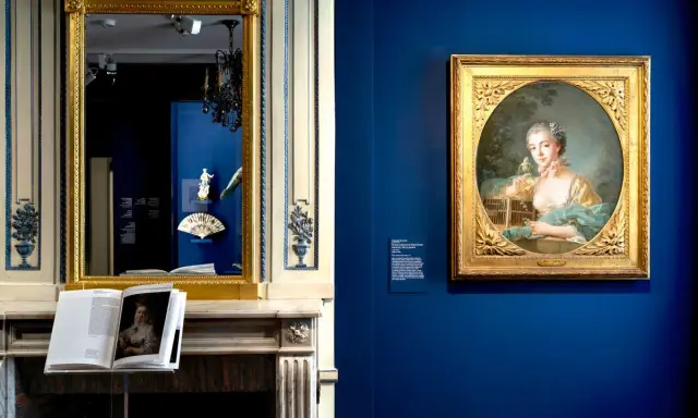 Portrait d'une jeune femme par un peintre français moderne, exposé dans un musée. Un livre ouvert sur une cheminée reflète l'œuvre.