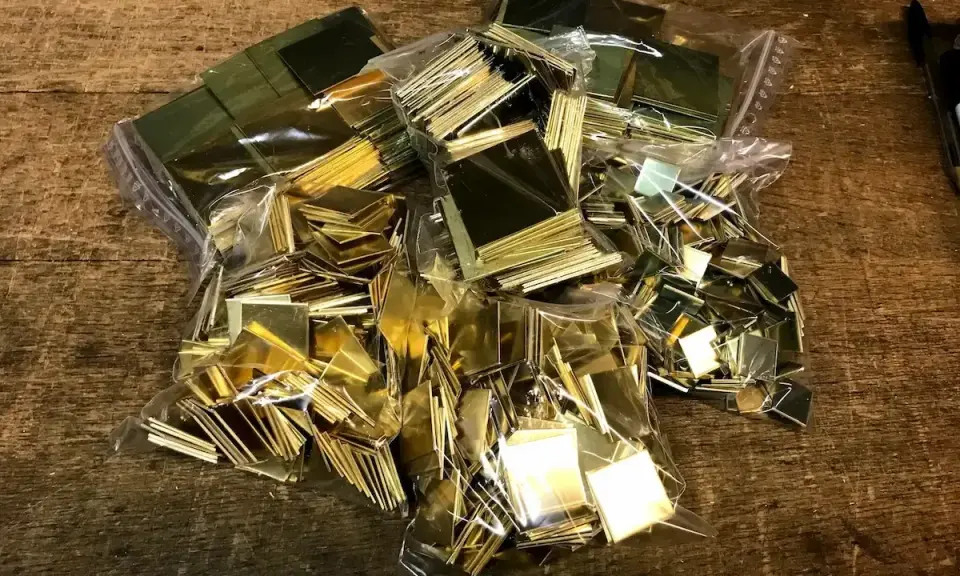 Des petits carrés de laiton brillants, prêts pour un projet de comment décaper du laiton. Ils sont dans des sacs en plastique sur une table en bois.