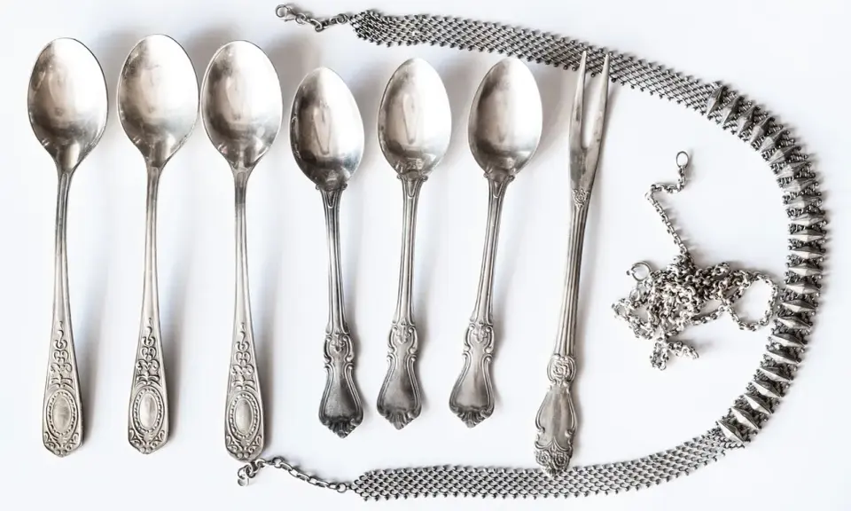 Six cuillères et une fourchette anciennes, ornées, sont disposées avec une chaîne argentée. Idéal pour apprendre comment nettoyer l'argenterie.