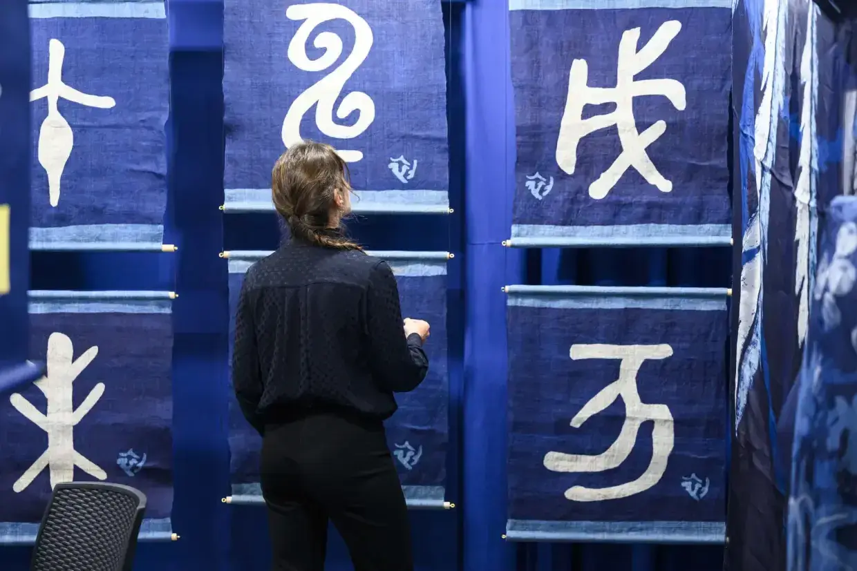 Une femme admire des bannières bleues ornées de calligraphies blanches lors d'un salon du patrimoine.