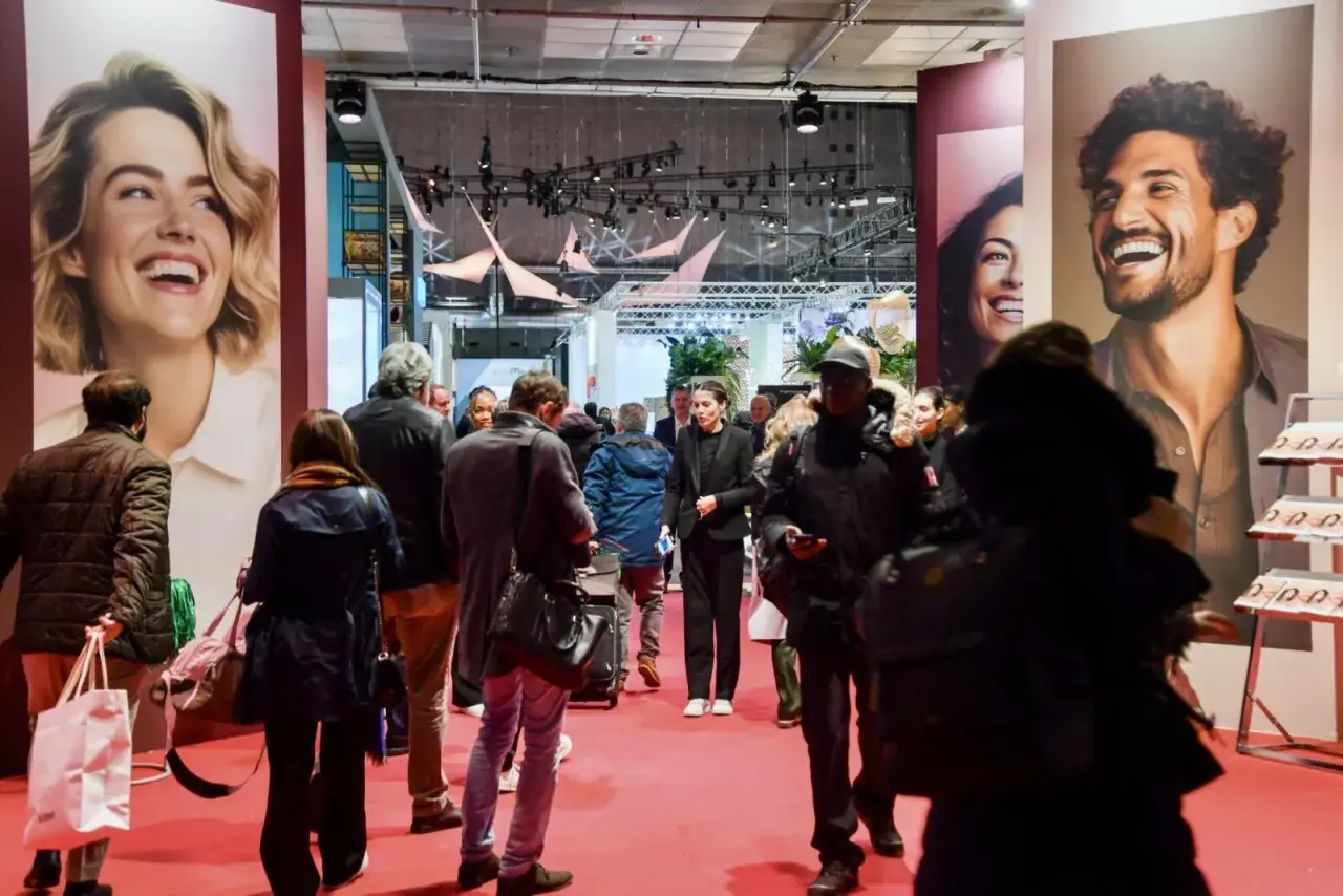 Foule dans un salon, devant de grandes affiches publicitaires. L'esprit meuble est palpable, les gens déambulent, curieux.