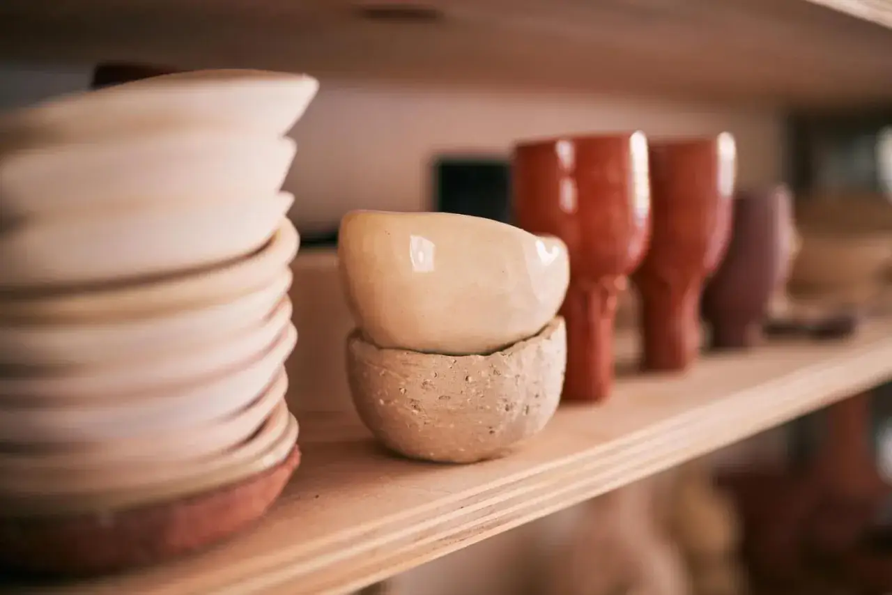 Sur une étagère en bois, des bols et des gobelets en terre cuite, œuvres d'un céramiste France, attendent d'être vendus.