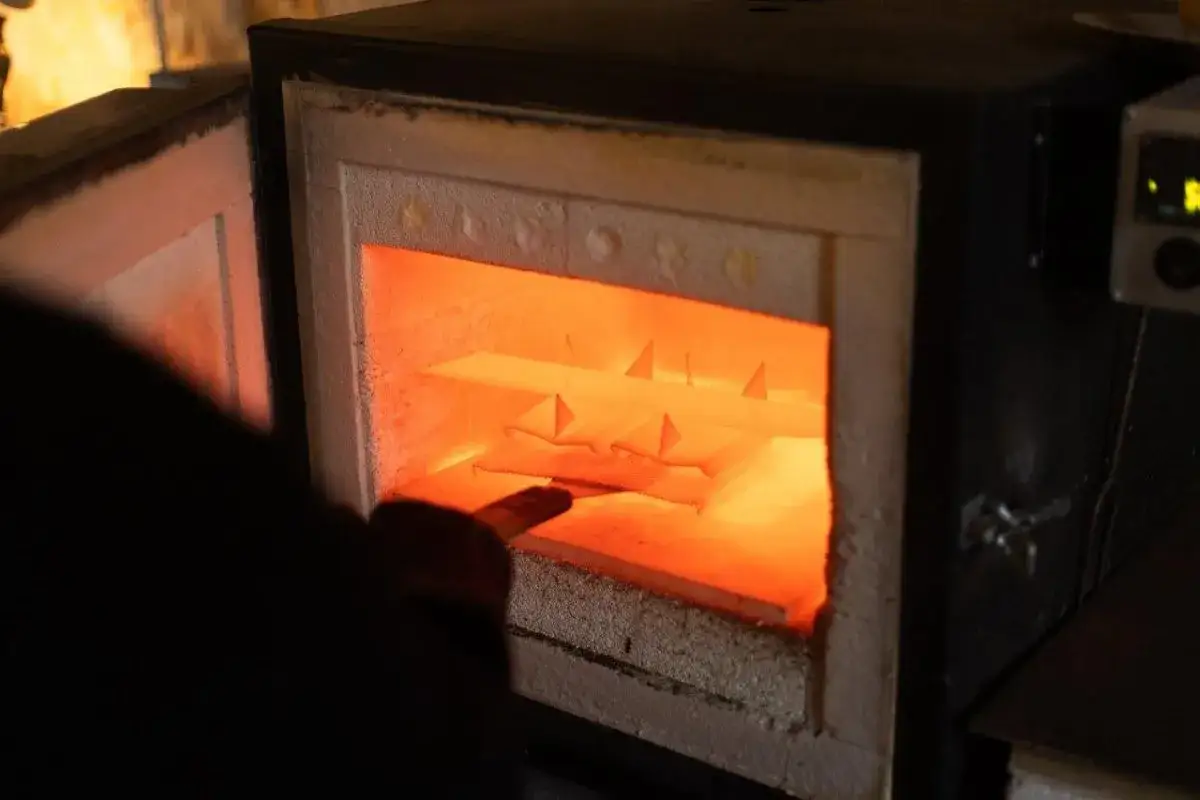 Un artisan &eacute;mailleur surveille des pi&egrave;ces dans un four incandescent. La chaleur intense r&eacute;v&egrave;le la magie de la transformation.