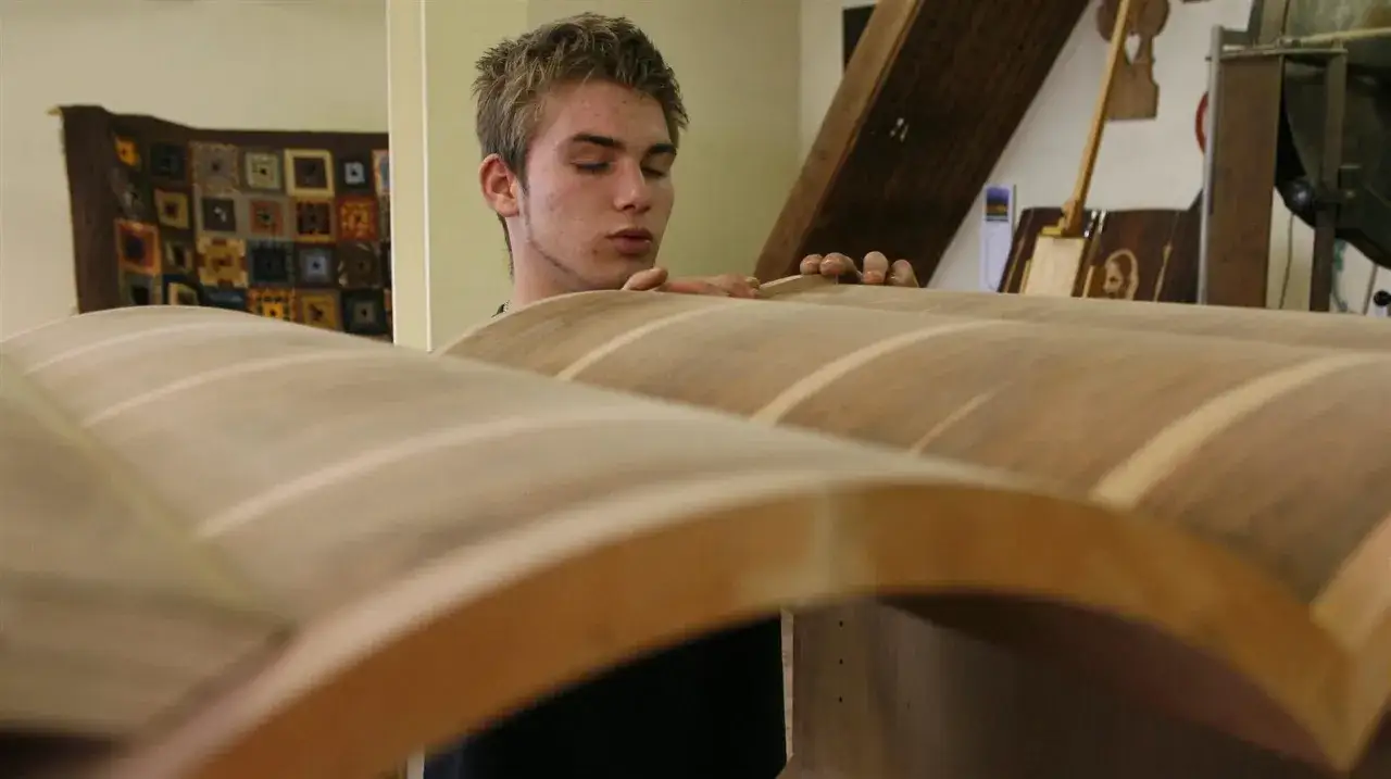 Un jeune homme apprend l'artisanat du bois, manipulant avec soin des pi&egrave;ces courb&eacute;es.