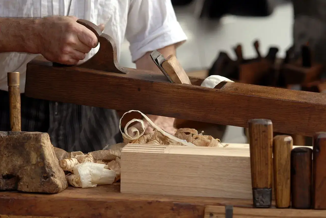 Un &eacute;b&eacute;niste travaille le bois avec un rabot, produisant des copeaux. Un m&eacute;tier d'art qui m&eacute;rite un bon &eacute;b&eacute;niste salaire.