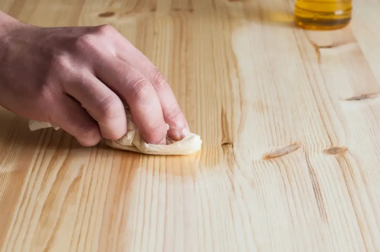 Main d'une personne nettoyant un meuble en bois cir&eacute; encrass&eacute; avec un chiffon imbib&eacute; de produit.