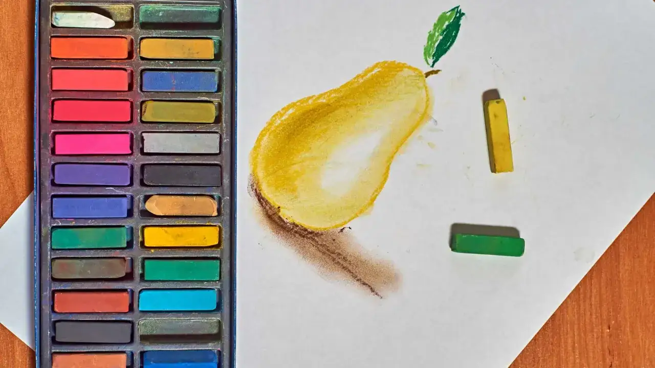 Une poire jaune est dessin&eacute;e &agrave; la technique pastel sec. &Agrave; c&ocirc;t&eacute;, une bo&icirc;te de pastels et quelques b&acirc;tonnets de couleur.