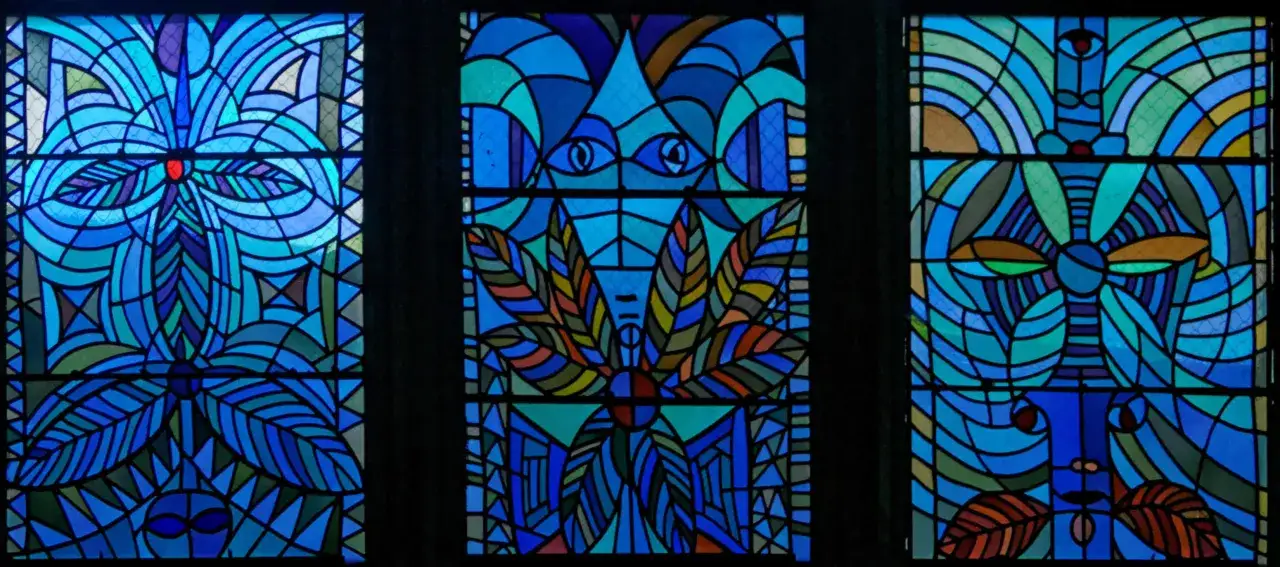 Trois vitraux aux motifs abstraits bleus et verts, évoquant des formes végétales et des visages stylisés, signés Cocteau à Metz.