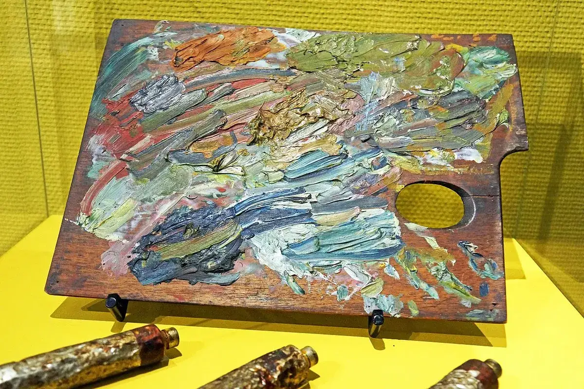 Palette d'artiste couverte de pigments synth&eacute;tiques, t&eacute;moignage d'une cr&eacute;ation vibrante. Des tubes de peinture usag&eacute;s reposent en avant-plan.