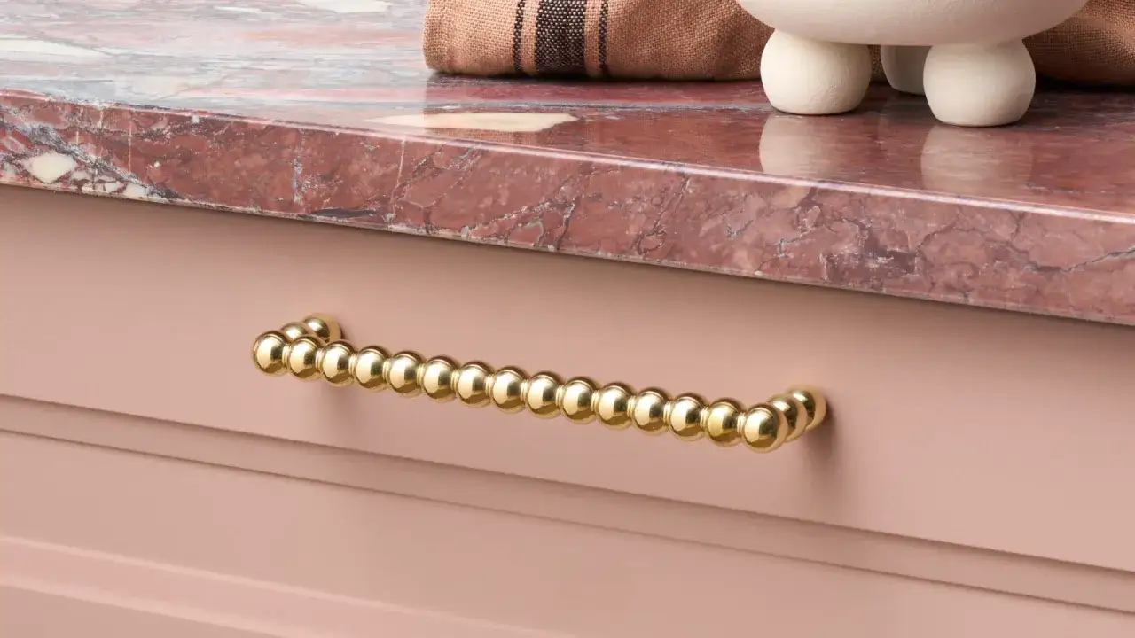 Poignée de tiroir en cuivre jaune, perles dorées sur fond rose. Apprenez comment nettoyer le cuivre jaune pour qu'il brille ainsi.