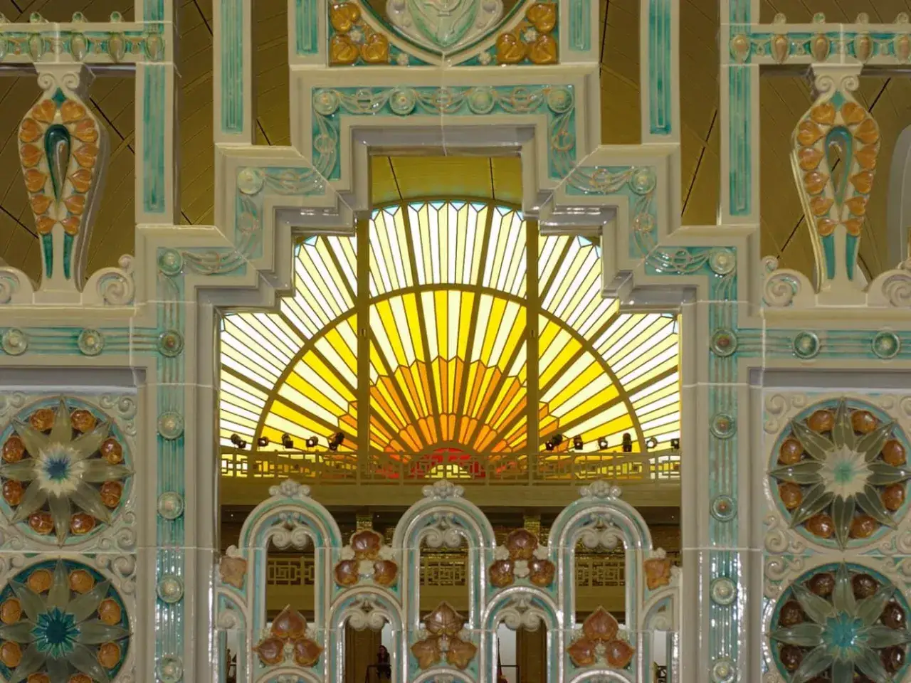 Ornementation art déco aux motifs floraux et géométriques, encadrant une verrière jaune rayonnante.