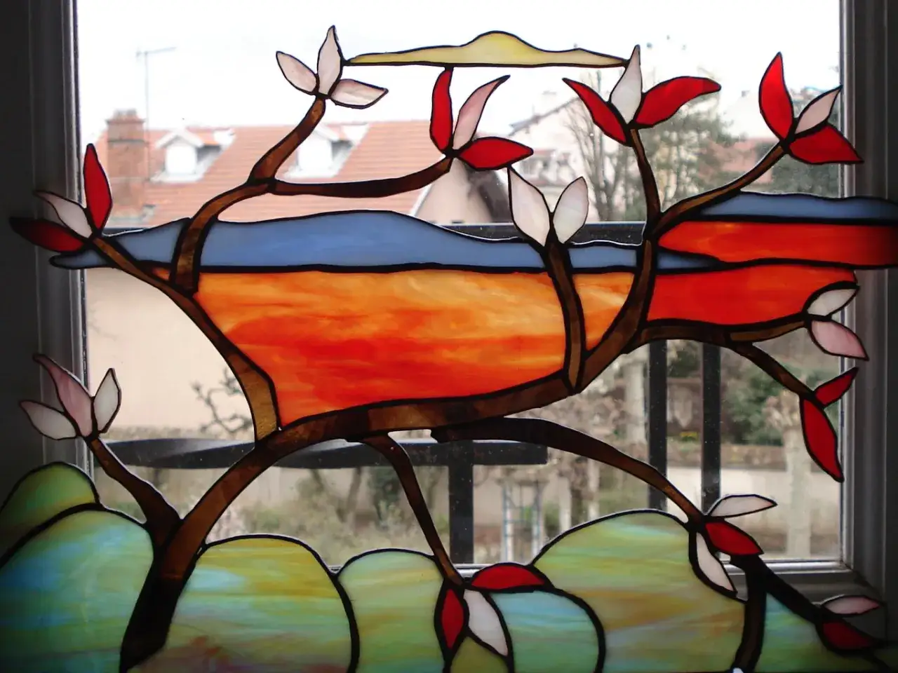 Vitrail aux couleurs chaudes, &eacute;voquant l'initiation de Tiffany. Branches stylis&eacute;es aux feuilles rouges et blanches, sur fond de ciel bleu et de paysage orang&eacute;.