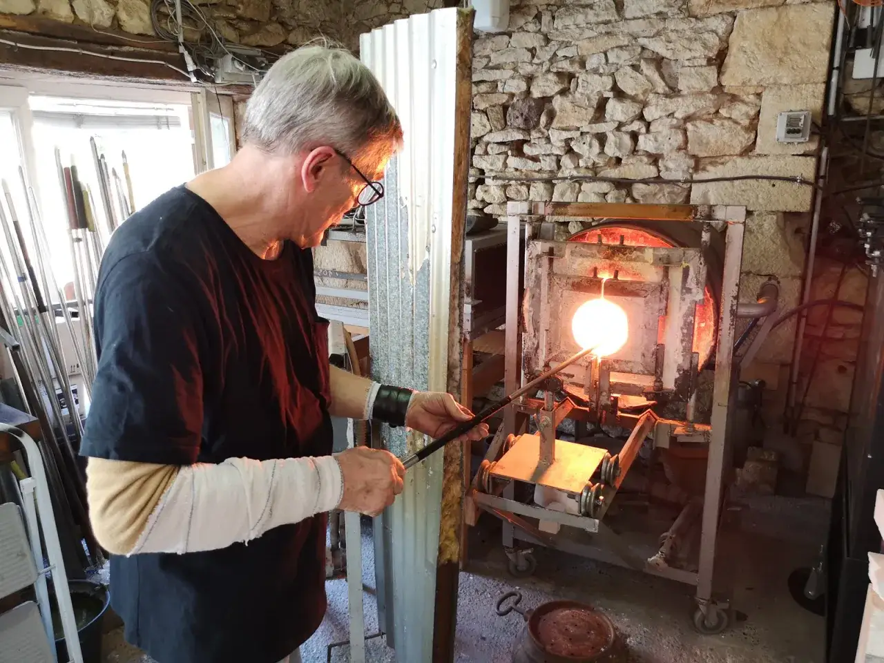 Un ma&icirc;tre verrier fa&ccedil;onne un objet en verre incandescent dans un four.