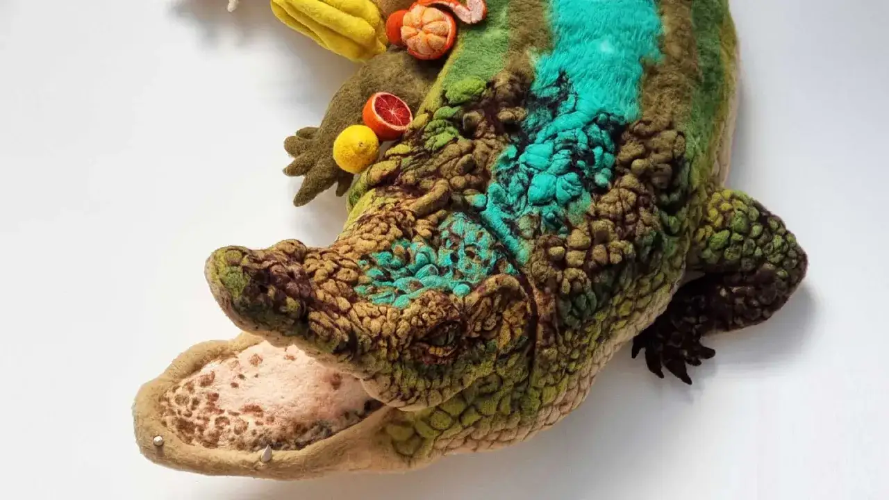 Un crocodile en feutre, œuvre d'un artiste textile, orné de fruits colorés. Ses écailles texturées et ses touches de turquoise évoquent une créature fantastique.