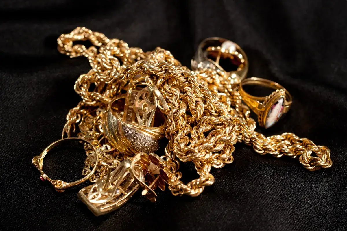 Montre comment reconnaitre de l'or sur une pierre : un amas de bijoux dorés, chaînes et bagues, sur fond noir.