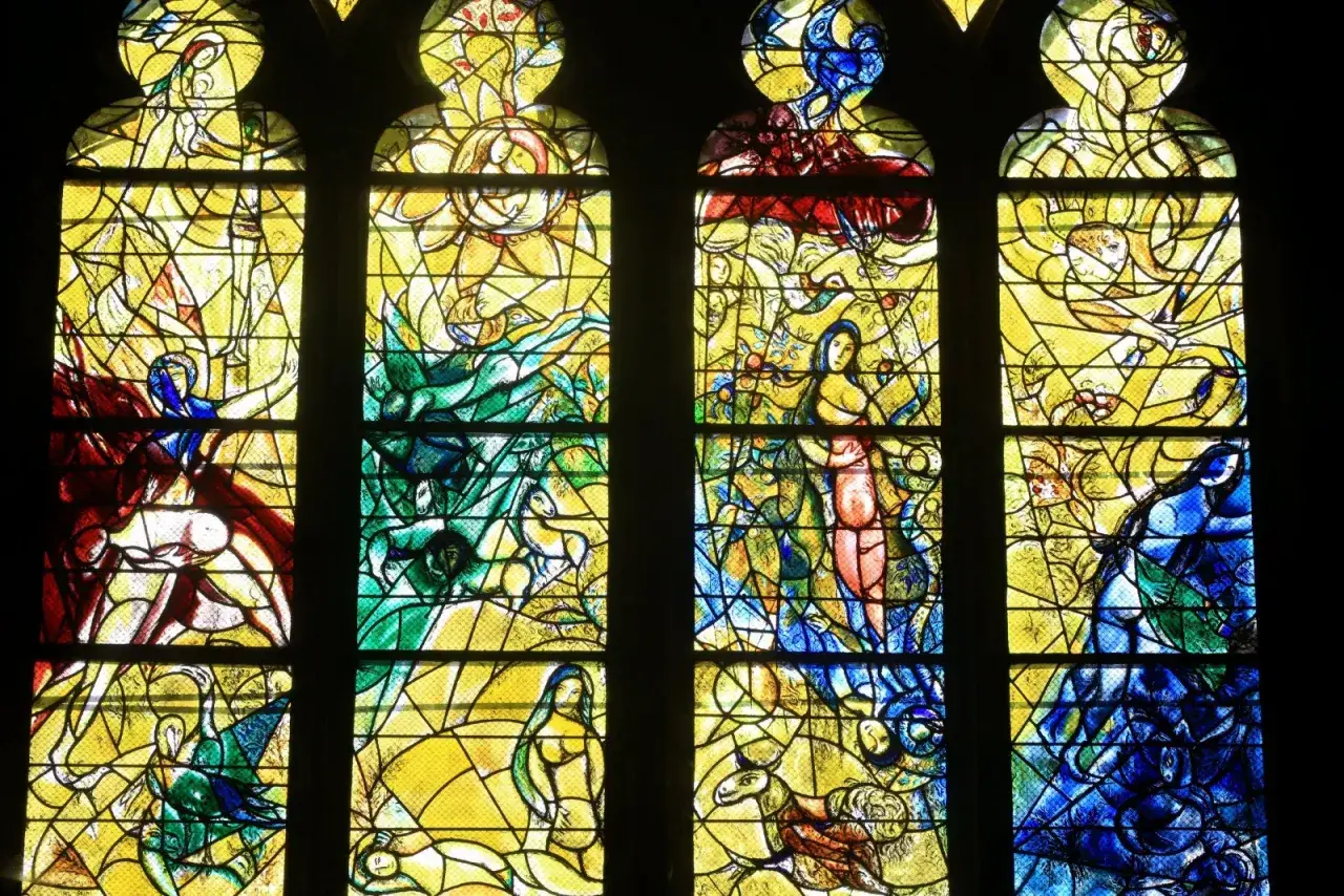 Vitraux de Chagall dans une église, représentant des scènes bibliques et des figures humaines dans des couleurs vives et un style unique.