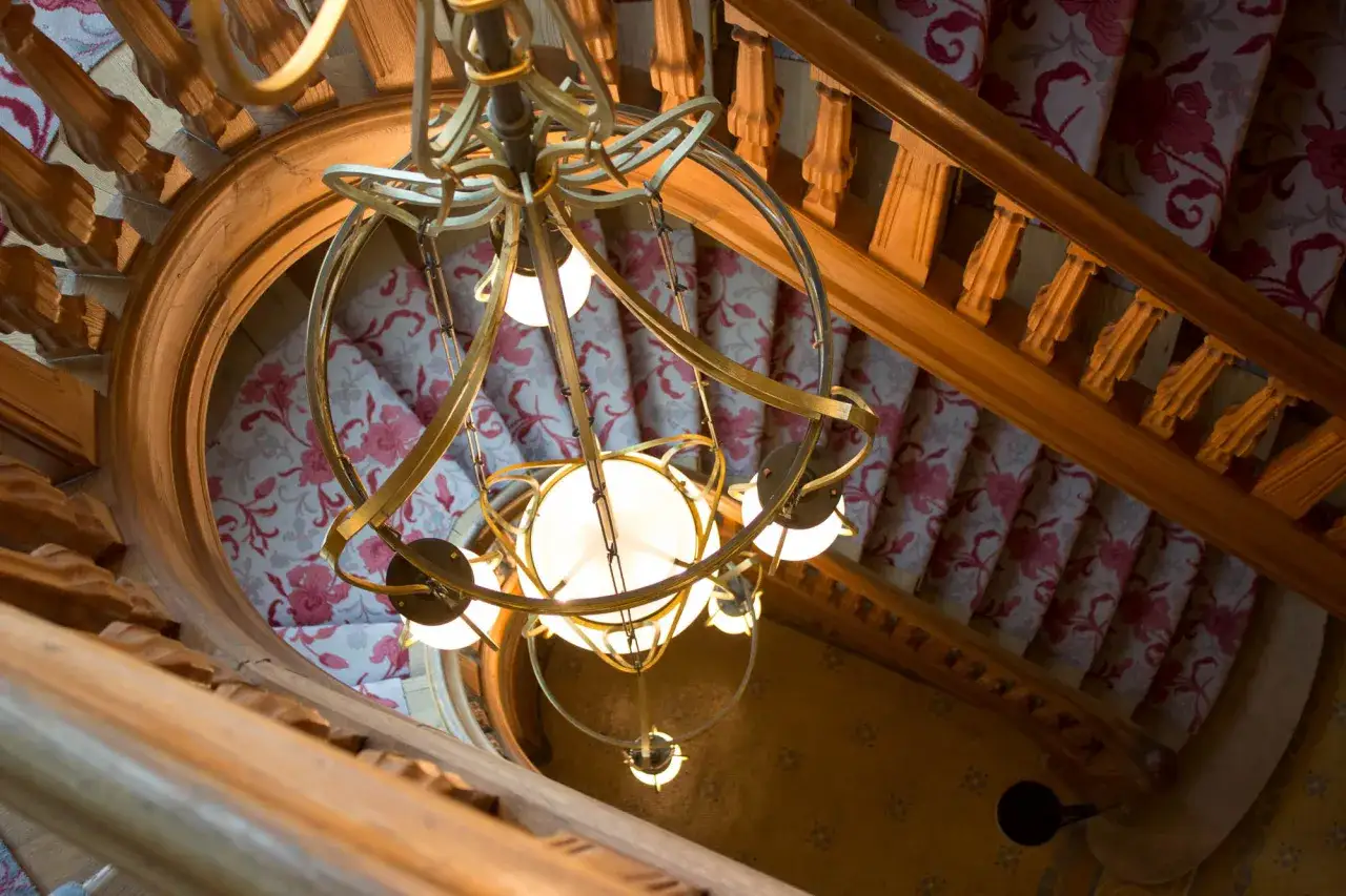 Lustre dor&eacute; au-dessus d'un escalier en colima&ccedil;on avec tapis fleuri, &eacute;voquant le charme de la villa Mademoiselle &agrave; Reims.
