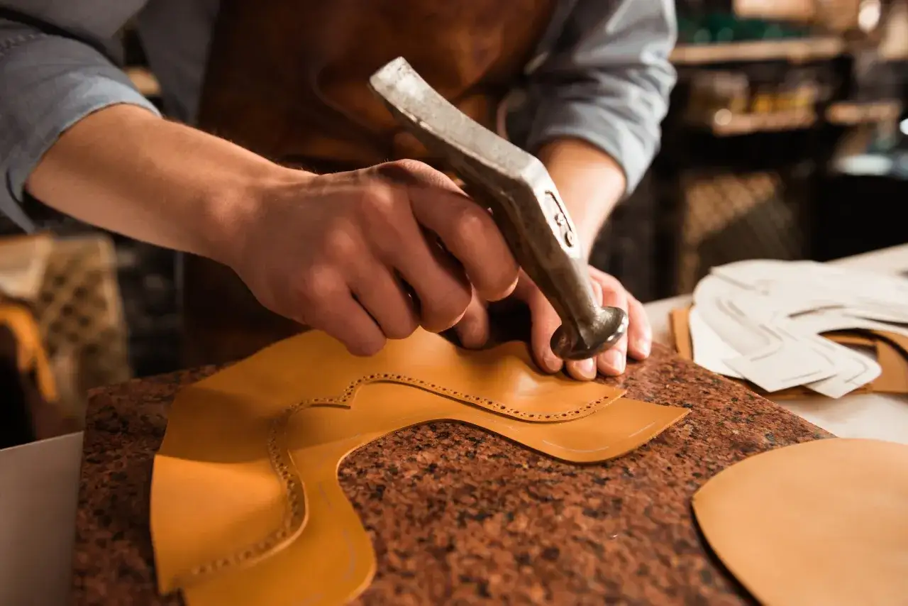 Artisan travaillant le cuir avec un marteau pour fa&ccedil;onner une pi&egrave;ce de chaussure. Le cuir souple est pr&ecirc;t pour la couture.