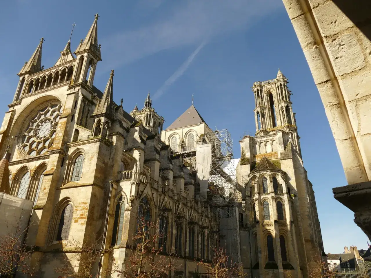 La cathédrale de Laon, majestueuse et ancienne, se dresse sous un ciel bleu. Des échafaudages entourent une partie de sa structure, témoignant de sa préservation.