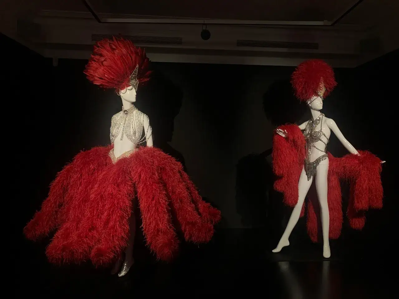 Deux mannequins portent des costumes de spectacle orn&eacute;s de plumes rouges, t&eacute;moignage du savoir-faire d'un artisan plumassier.