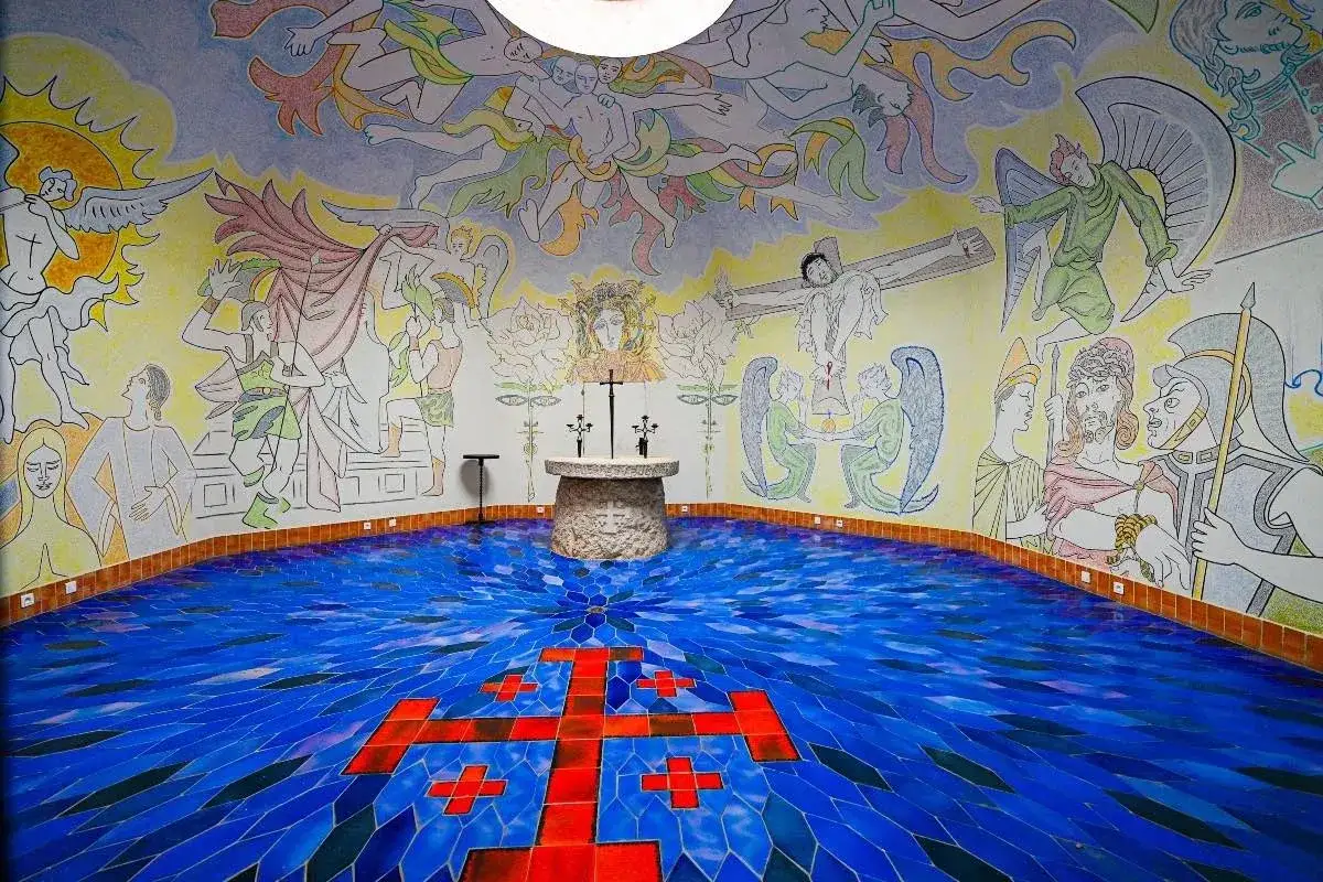 Chapelle ornée de fresques colorées par un peintre religieux contemporain, représentant des scènes bibliques et des anges. Le sol bleu est orné d'une grande croix rouge.