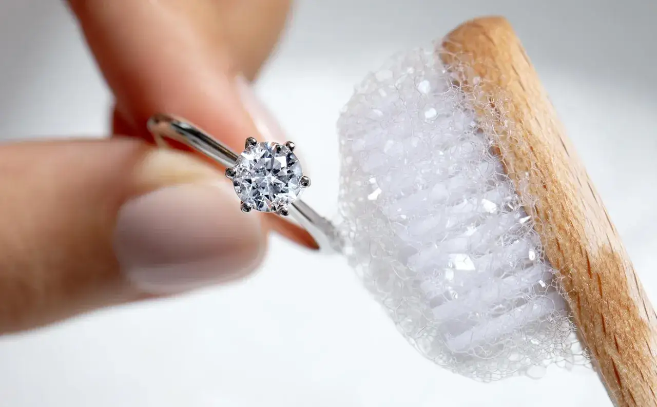 Une bague avec un diamant est tenue près d'une brosse à dents savonneuse, montrant comment nettoyer des diamants pour leur redonner leur éclat.