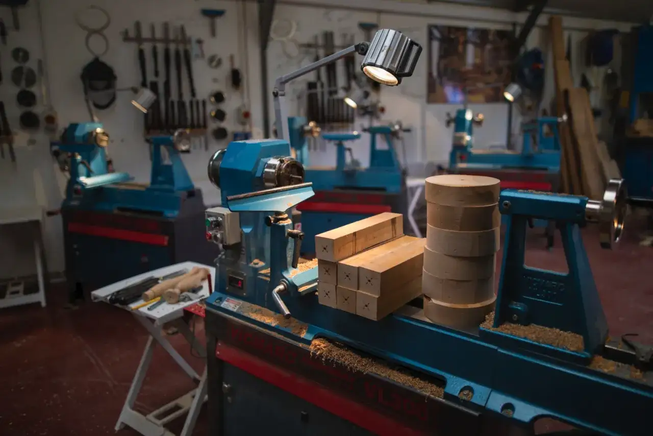 Atelier de tournage sur bois avec plusieurs tours bleus, des blocs de bois et des outils.