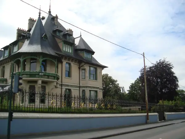 La maison Demoiselle à Reims, une bâtisse de style Belle Époque avec ses toits pointus et sa ferronnerie verte. Le mot "CHAMPAGNE" est visible sur la grille.