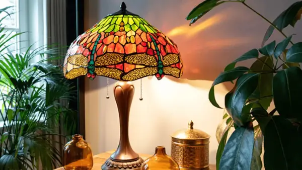 Lampe tiffany origine, abat-jour en vitrail coloré avec libellules, sur une table en bois avec des plantes.