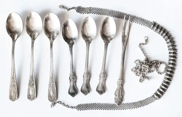 Six cuillères et une fourchette anciennes, ornées, sont disposées avec une chaîne argentée. Idéal pour apprendre comment nettoyer l'argenterie.