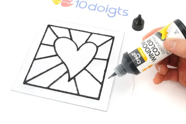 Main noire pour un modèle vitrail en forme de cœur. Un tube de peinture contour est tenu par une main.